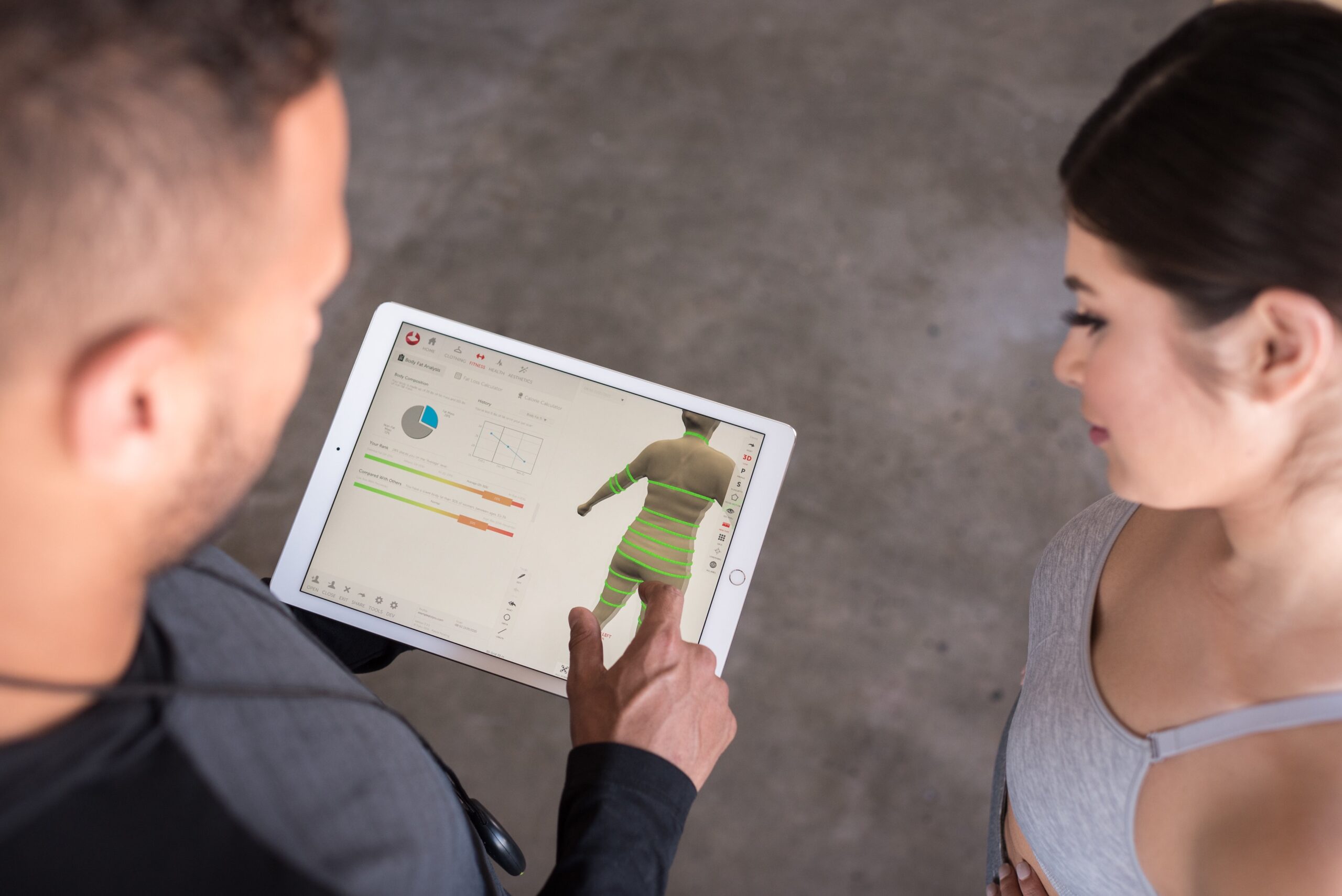 Styku promotional photograph showing a coach and client reviewing a 3D body model and measurements on a tablet
