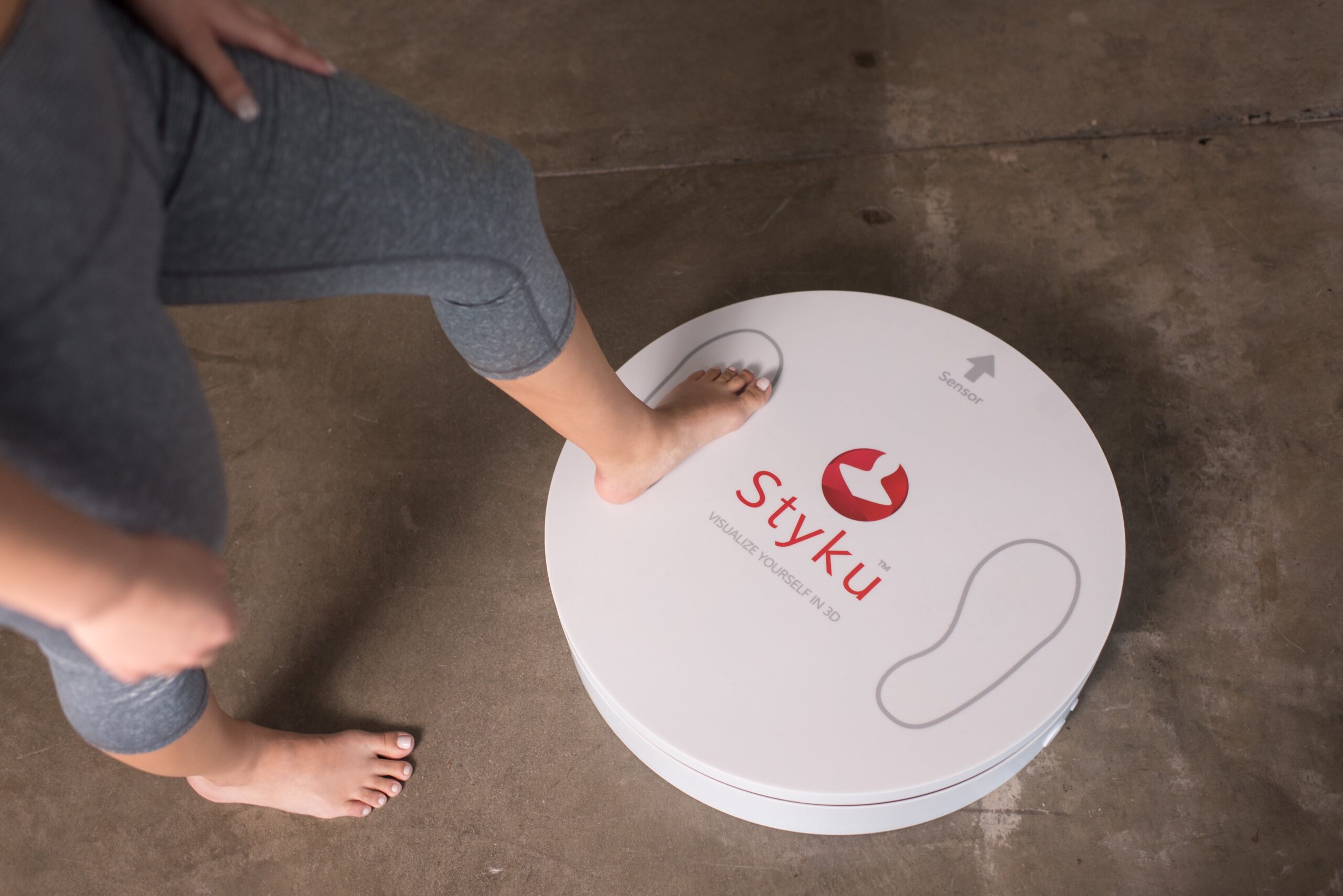 A person stepping onto the marked footprints on a Styku scanning platform